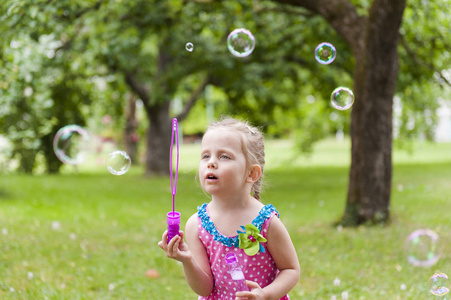 一个穿着五颜六色衣服的小女孩在夏日公园里吹肥皂泡