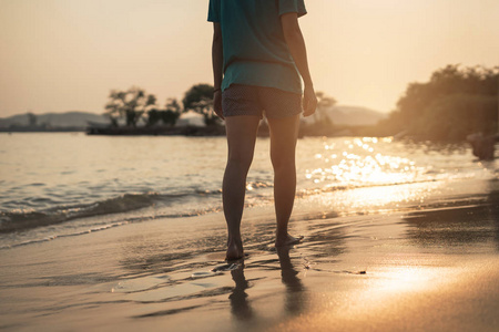 年轻女人旅行海滩上散步，在美丽的日落