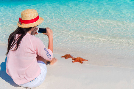 女人用手机拍照红海星热带海滩上