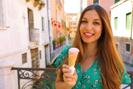 意大利威尼斯的绿色连衣裙的微笑的旅游女孩吃冰淇淋