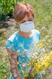 戴着保护面具的妇女捧着野花, 试图抗击对花粉的过敏。自然光。过敏概念