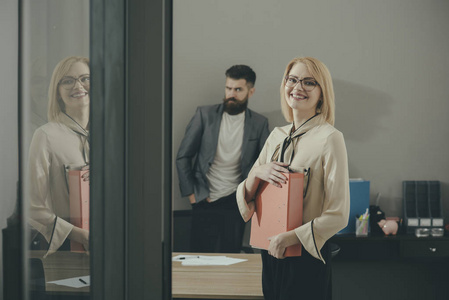 在办公室的背景快乐的女人和大胡子男子。企业妇女微笑与文件文件夹。交易前的文书工作。合同的最佳条件。在工作中有信心和成功的同事