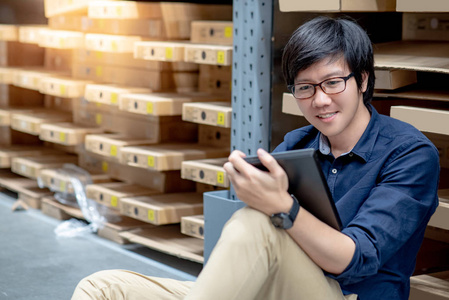 亚洲年轻人用数码片在仓库货架上的纸板箱里清点产品。物理库存盘点概念