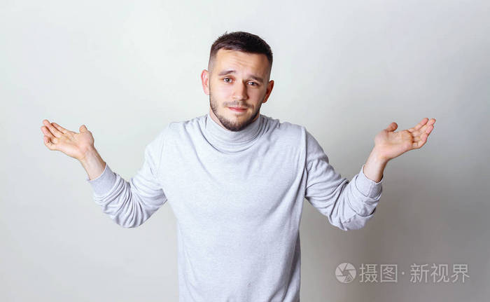 男子在白色的高领毛衣举起手 耸耸肩他的肩膀上灰色背景复制空间
