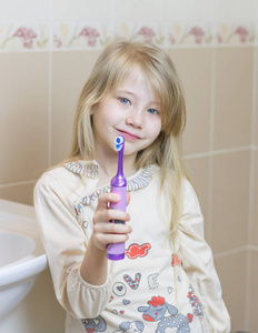 漂亮的女孩在浴室里显示一把电动牙刷