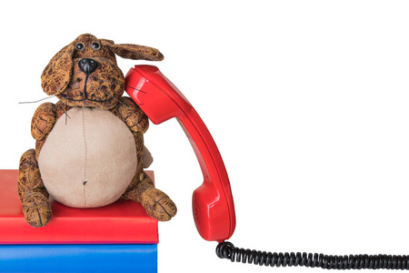 红色老式电话接收机与黑色电缆隔离在白色背景。滑稽的狗坐在书上并打电话。适用于联系交流和呼叫中心。产品展示蒙太奇模板