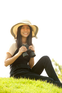 漂亮的亚洲年轻女子坐在土墩上寻找望远镜。