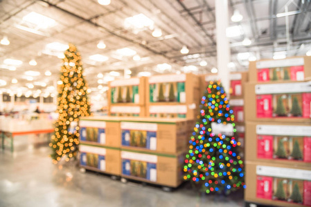 模糊的图像巨大的圣诞树装饰批发商店。散景灯的花环和琴弦环绕着人造圣诞树。圣诞装饰品展示在美国销售