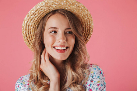 关闭在夏季礼服和稻草帽子的一个快乐的年轻女子的肖像看着远离粉红色背景的孤立