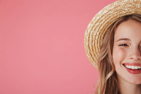 关闭半脸肖像的一个快乐的年轻女子在草帽看着相机与复制空间的粉红色背景隔离