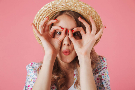 关闭一个开朗的年轻女子在夏季礼服和草帽显示确定的姿态, 在粉红色背景下隔离的肖像