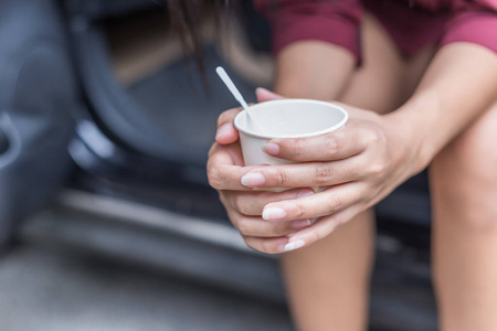女人坐在汽车旁边，拿着一次性杯咖啡