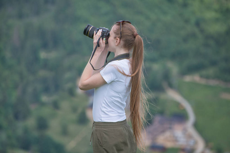 女孩与照相机站立在山和摄影自然。背景林