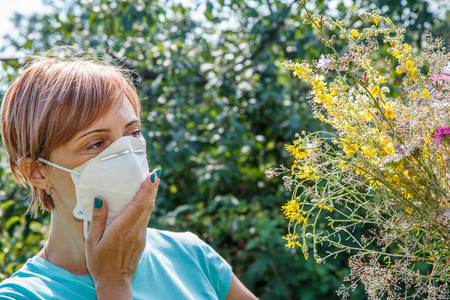 戴着保护面具的妇女捧着野花, 试图抗击对花粉的过敏。妇女保护她的鼻子从过敏原