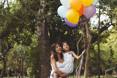 幸福的母亲和女儿在公园与彩色气球
