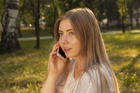 年轻美丽的金发女孩说手机和微笑, 在公园的电话交谈