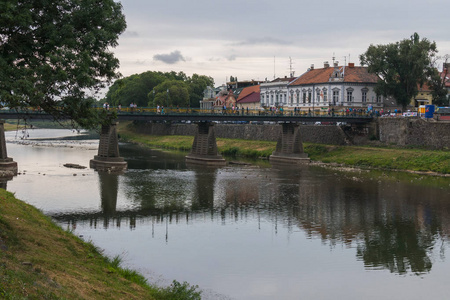 一座横跨河流的大型行人桥, 许多人沿着它和河堤漫步。以古建筑为背景的房屋