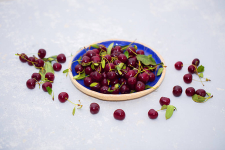 食物照片。新鲜成熟的樱桃在一个盘子里和在一张桌子上的光背景。野生浆果, 健康维他命和夏日概念