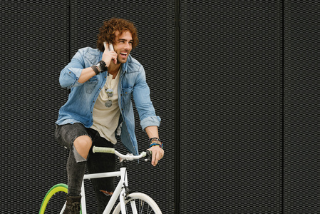 英俊的年轻男子，与移动电话和固定的齿轮自行车