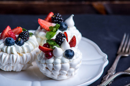 精致的白色蛋白甜饼与新鲜的浆果在盘子里。甜点帕夫洛娃特写。黑暗的背景。喜庆的婚礼蛋糕