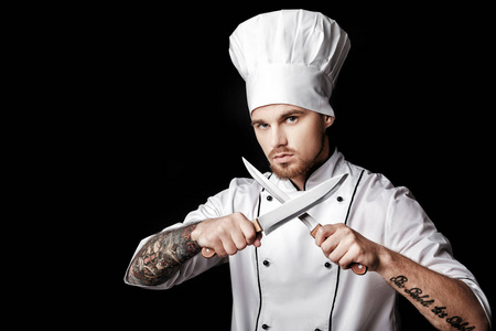 年轻胡子男人厨师在白色均匀搁置在黑色背景上的两把刀