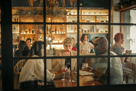 一群不同的年轻朋友坐在一起, 在一个时髦的酒吧在一个桌子的窗口聊天和享受饮料