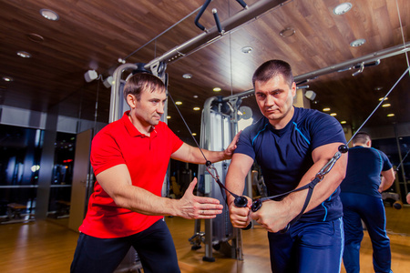 私人教练帮助男性在健身房举重室工作