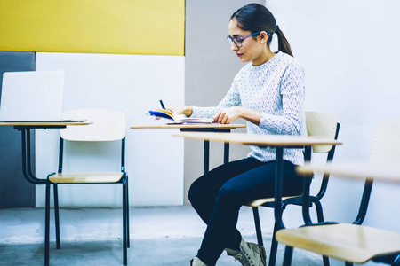 集中聪明的女学生坐在书桌在教室准备考试在大学, 聪明的年轻妇女做笔记为课程计划花费时间在天生