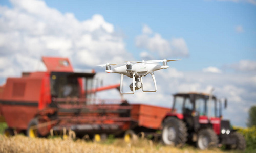在早期的夏季, 在拖拉机前飞行的无人机与向日葵田联合收割机。农业技术创新