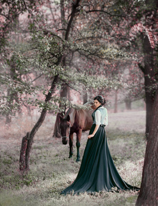 一位穿着老式连衣裙的年轻女士用她的马在森林里漫步。女孩有白色上衣, jabot, 领带, 灰色背心, 黑色长裙和火车。一个古老的