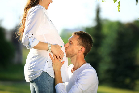 幸福的丈夫拥抱他怀孕的妻子在公园里散步