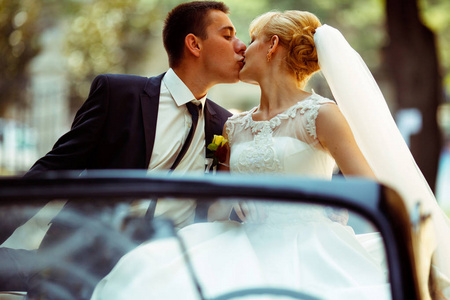 未婚夫吻漂亮金发新娘坐在一辆黑色的车子
