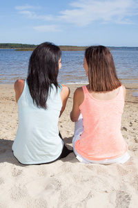 两个适合的年轻女子坐在沙滩上的春季假期