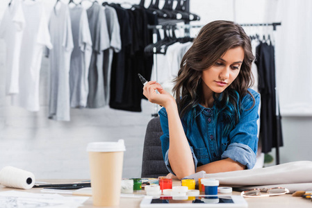 服装设计工作室中的女时装设计师在工作桌上的夹克上涂上咖啡杯