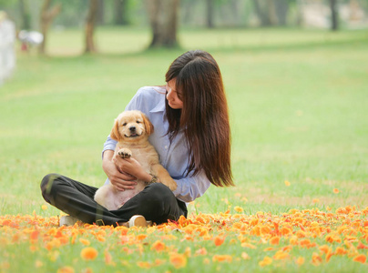 美丽的年轻亚洲妇女玩一个可爱的金色猎犬狗在公园