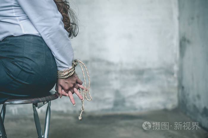 女人的手绑着.妇女被戴上手铐, 坐在椅子上. 女人把手绑在椅子上.