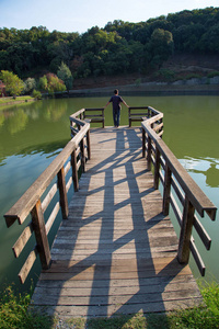 站在木码头边缘的人的后方观在阳光明媚的秋日望着平静的湖面