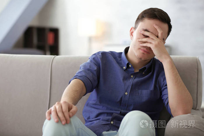 英俊的郁闷的男人在家里的沙发上