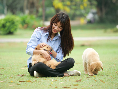 美丽的年轻亚洲妇女玩一个可爱的金色猎犬狗在公园