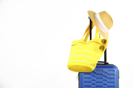 单蓝色塑料硬壳行李与妇女的草帽悬挂在扩展伸缩手柄, 黄色沙滩袋, 太阳镜。一个手提箱准备度假旅行。白色背景, 复制空间