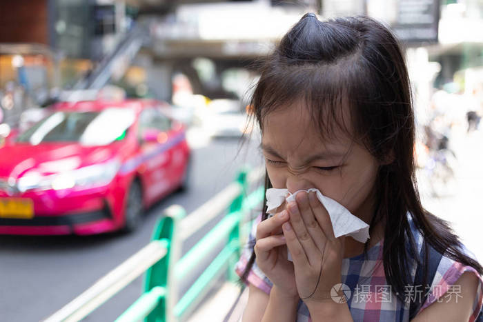 肖像可爱的小女孩吹鼻子在纸手帕, 亚洲女孩打喷嚏在一个组织在城市