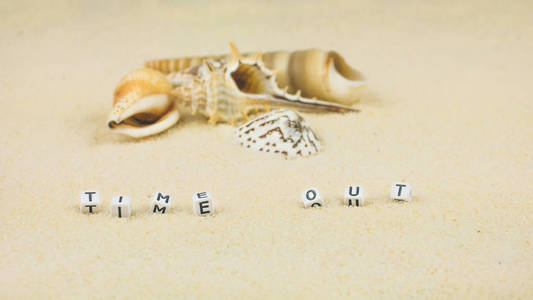 时间出字母前面海贝壳和彩色 wristbandon 在沙滩上。扁形