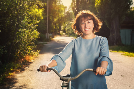 快乐的年轻女子走在乡间小路上的一辆自行车旁, 夕阳下的阳光下。色调