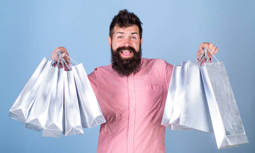 在销售旺季购物的家伙打折。销售和折扣的概念。在快乐的脸上的时髦是购物上瘾的人或购物狂。胡子和胡子的人举行购物袋, 浅蓝色背景