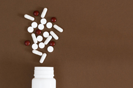 白色和褐色的药片从一个白色塑料瓶洒在一个空褐色的背景上。天然药物。复制空间