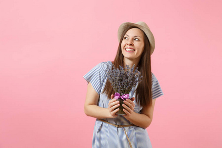 一个快乐年轻的温柔的女人在蓝色的礼服, 帽子捧着美丽的紫色薰衣草花在明亮的趋势粉红色背景上的花束。国际妇女节节日概念