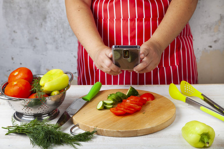 穿着红色围裙的女人在厨房的电话里拍照食物。