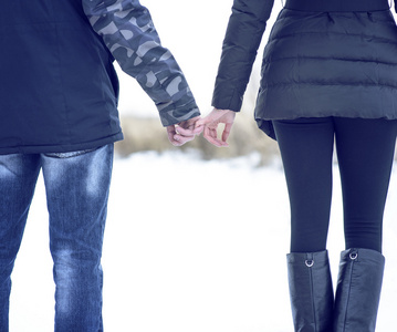 年轻的夫妇在户外，牵着双手在冬季公园。感人的年轻，家庭