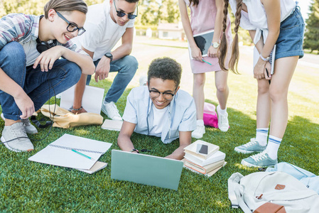 快乐的多民族青少年学生在公园里学习书籍和数字设备