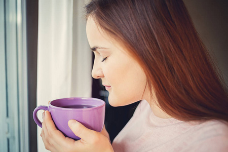 年轻女人享受杯茶在窗口附近早上